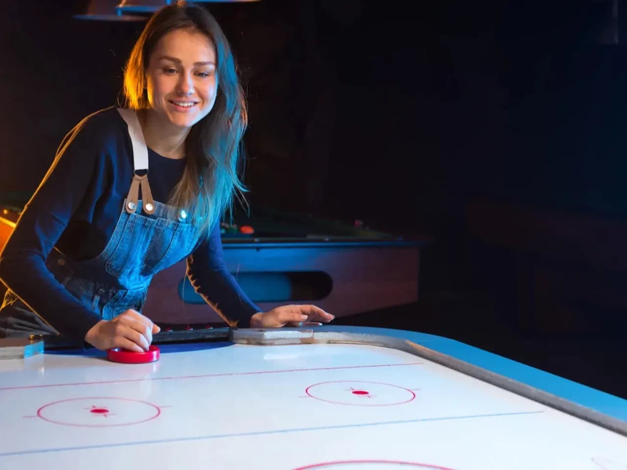 Гость играет в аэрохоккей за игровым столом в тёмной зоне