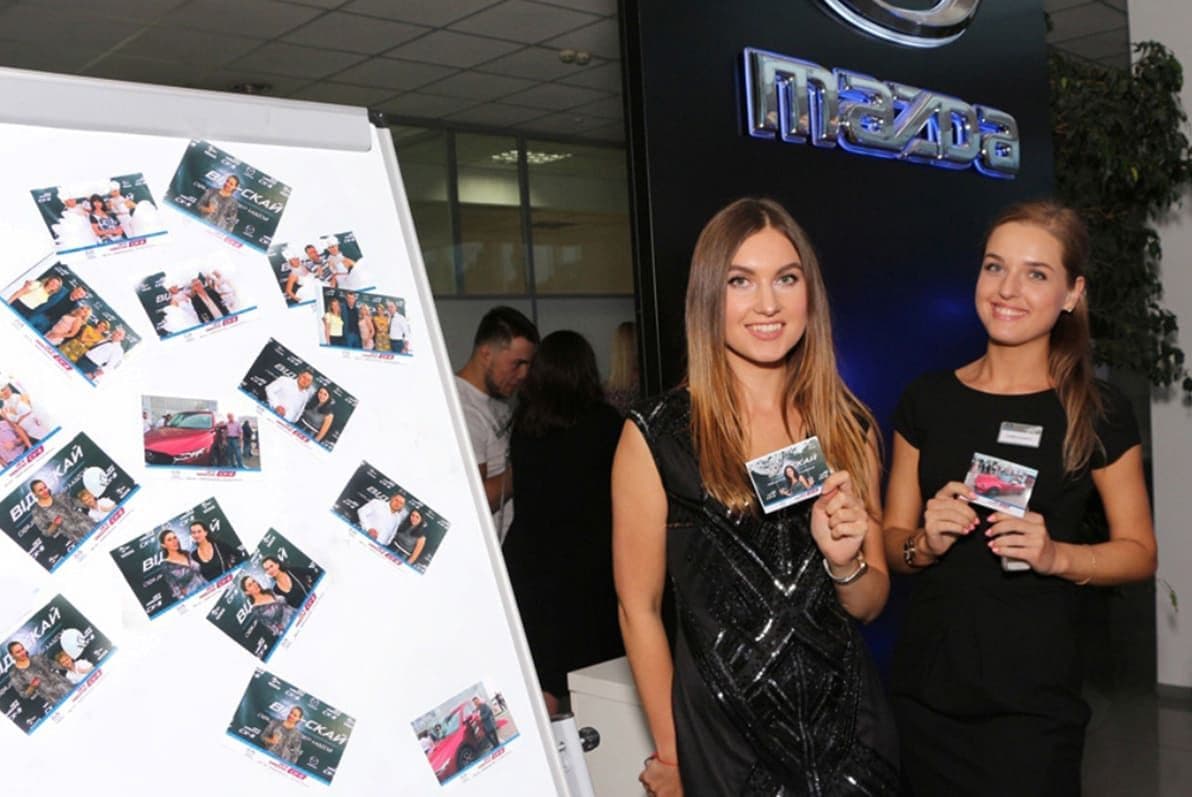 Гости демонстрируют фотографии из фотобудки возле панели для фото